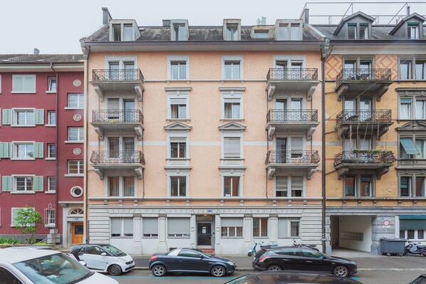 Un edificio a più piani con balconi, un ingresso a livello strada e auto parcheggiate.