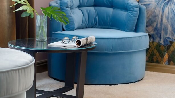 A modern living room with a blue armchair, a glass coffee table, a plant, and a large TV mounted on the wall. - VISIONAPARTMENTS Zurich Albertstrasse (Zürich)
