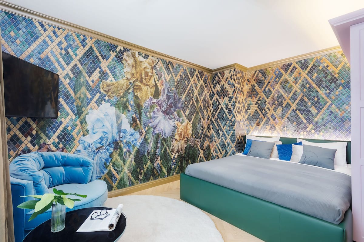 A bedroom with a blue sofa, a green bed, and a patterned wall.