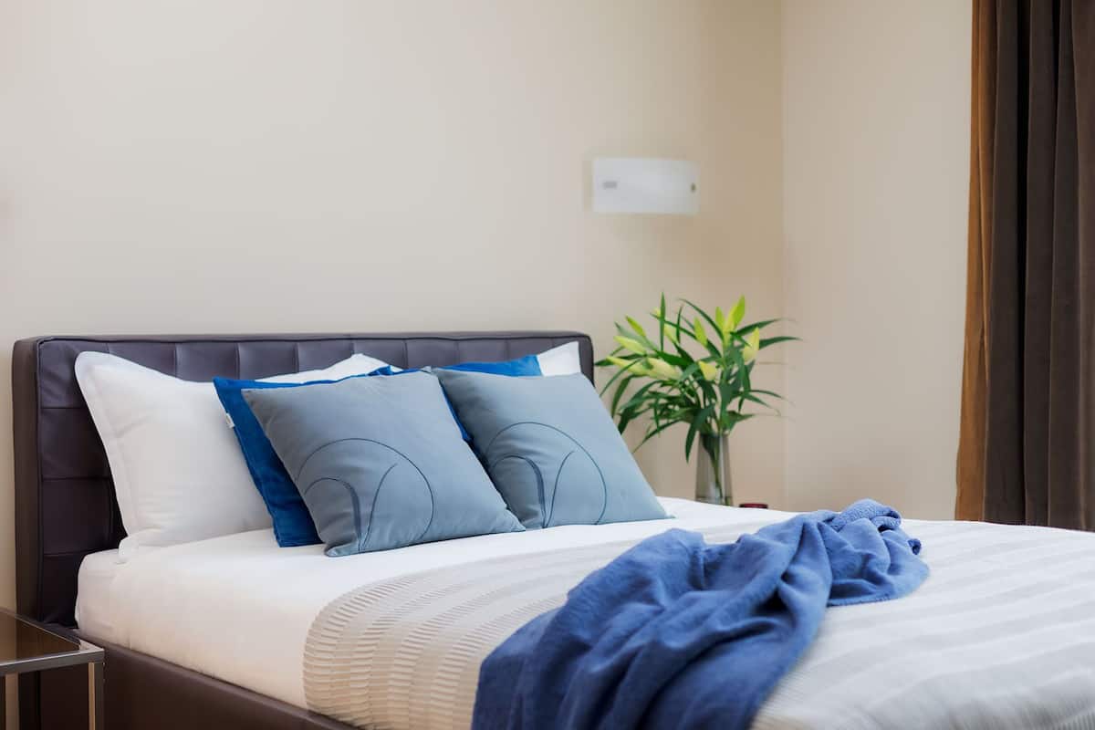 A neatly made bed with a white and blue bedding set, a dark headboard, and a blue throw blanket.