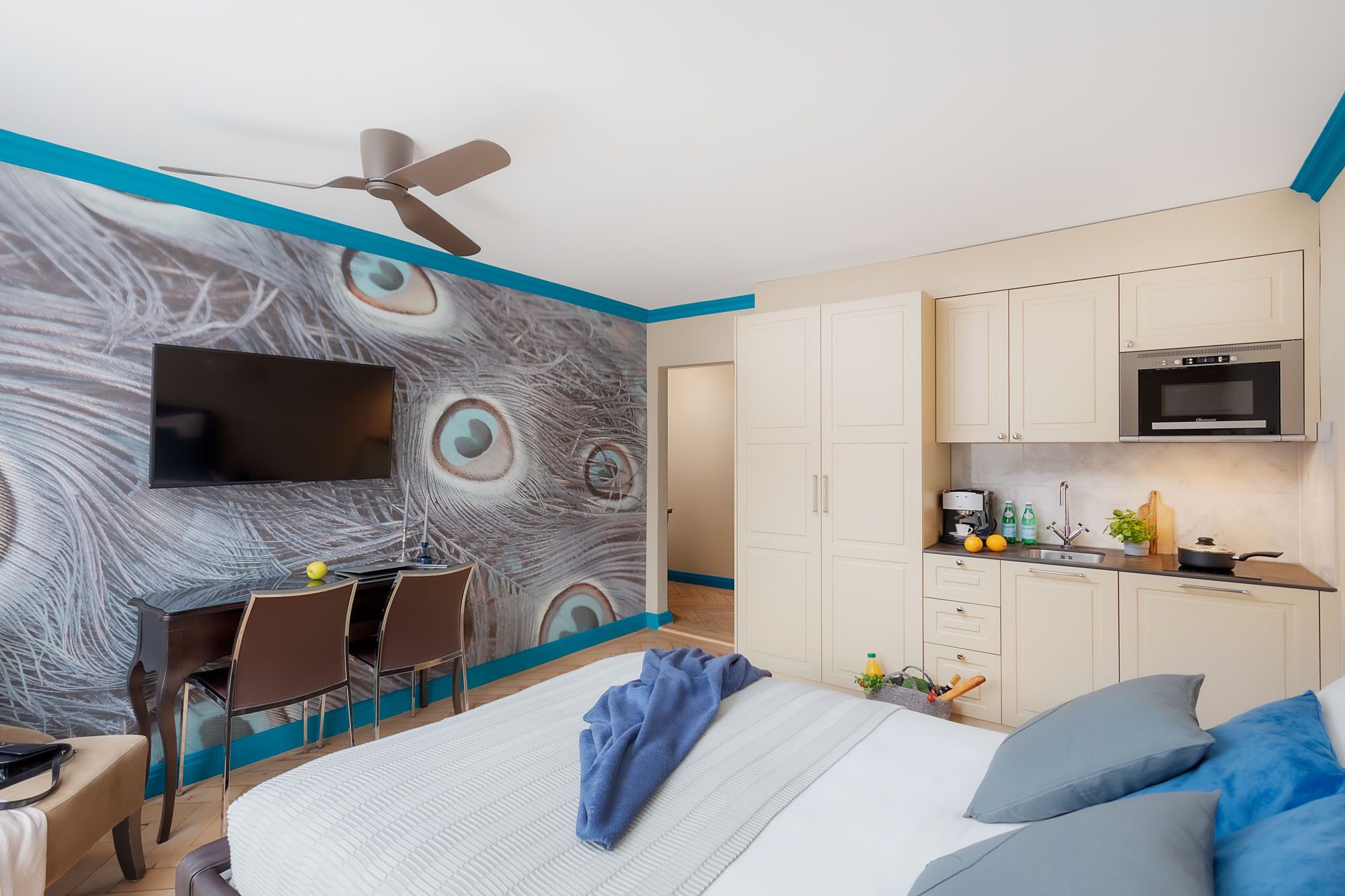A modern hotel room with a large bed, a desk, and a kitchenette.