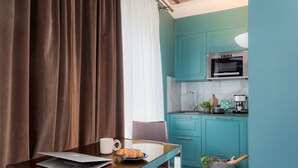 A modern kitchen with teal cabinets, a microwave, and a coffee maker. There's a laptop on a glass table with a plate of food and a mug. - VISIONAPARTMENTS Zurich Albertstrasse (Zürich)
