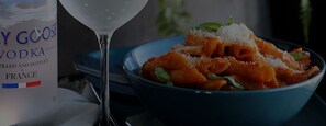 Una bottiglia di vodka Goose e una ciotola di pasta con un bicchiere d'acqua.