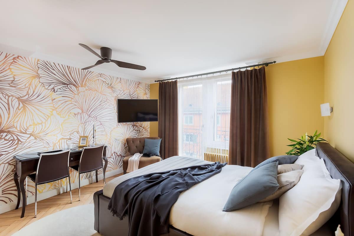 A bedroom with a bed, a desk, a chair, a ceiling fan, and a TV.