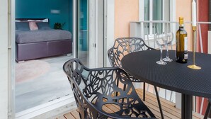 An open sliding door leading to a bedroom with a bed and a sofa, a balcony with a table and chairs, and a bottle of wine on the table. - VISIONAPARTMENTS Zurich Albertstrasse (Zürich)