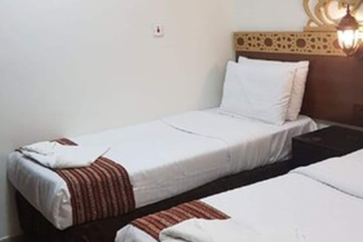 A hotel room with two single beds, a ceiling air conditioner, a wall socket, and a decorative wall lamp.