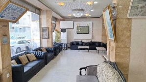 En lobby med en sort lædersofa, en grå sofa og et lille bord. Der er et fjernsyn monteret på væggen og en lysekrone i loftet.
