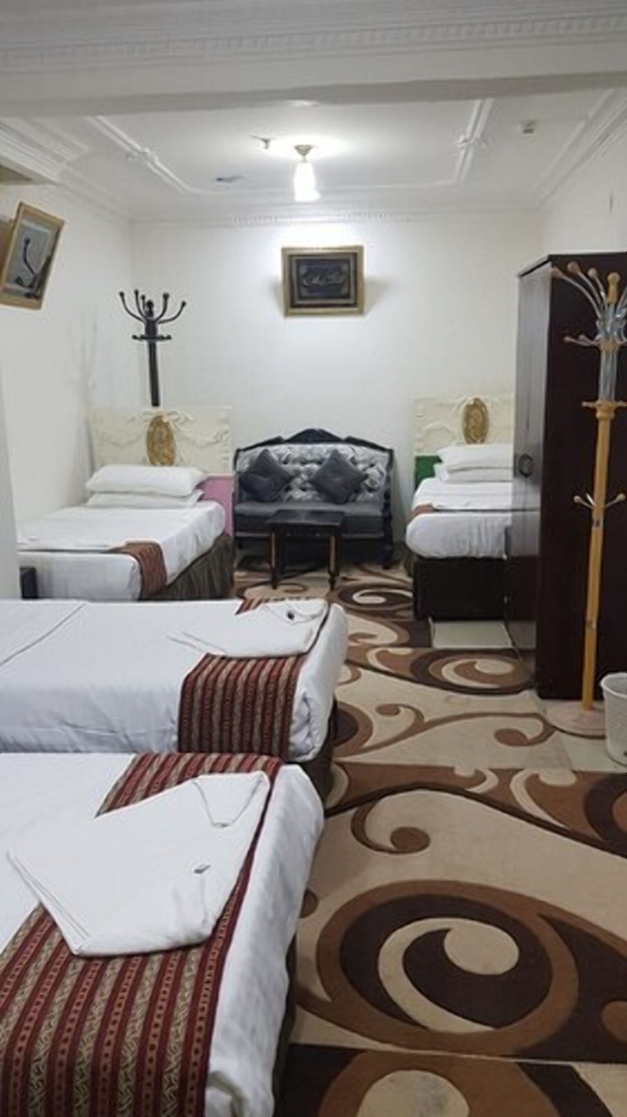 Una habitación de hotel con tres camas, un sofá, un armario y una alfombra decorativa.