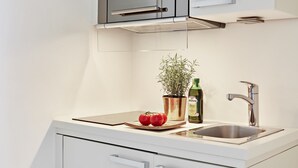 A modern kitchen with white cabinetry, a stainless steel sink, a microwave, and a potted plant.
