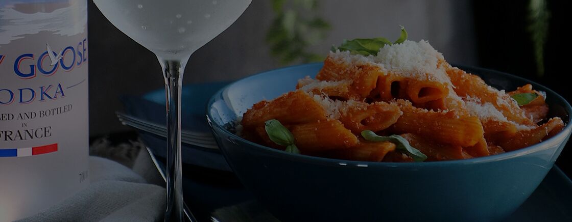 A bottle of Goose vodka and a bowl of pasta with a glass of water.