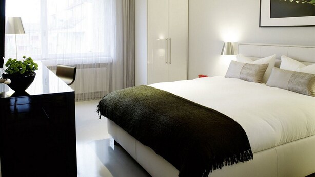 A modern hotel room with a large bed, a desk, and a window with curtains.