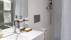 A modern bathroom with a white sink, mirror, towel rack, and shower.