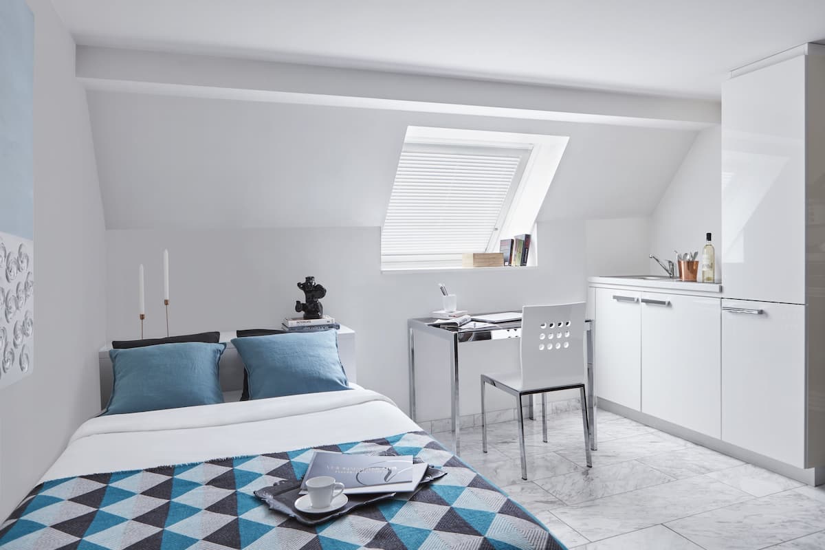 Un dormitorio moderno y compacto con tragaluz, una cama bien hecha, un escritorio pequeño y una silla.