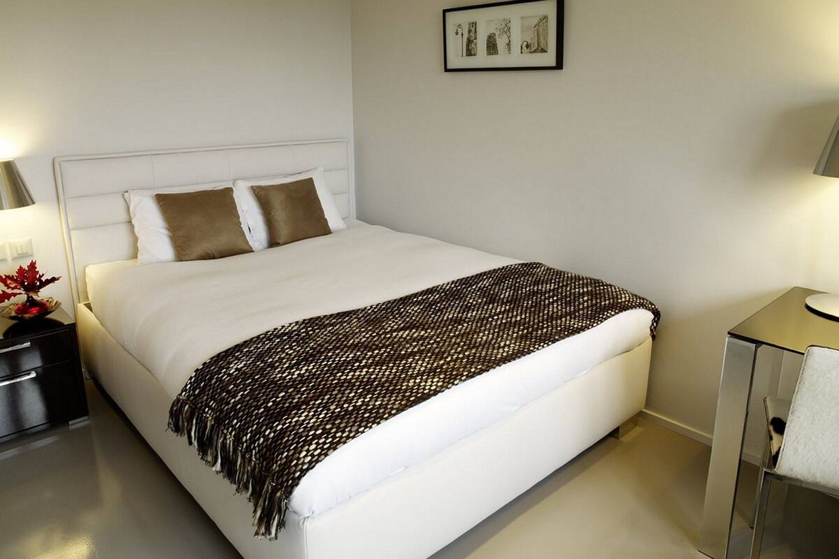 Una cama bien hecha con un cabecero blanco, una manta marrón y un cuadro colgado encima.