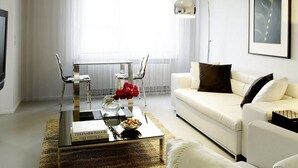 A modern living room with a glass coffee table, white sofa, and a framed picture on the wall.