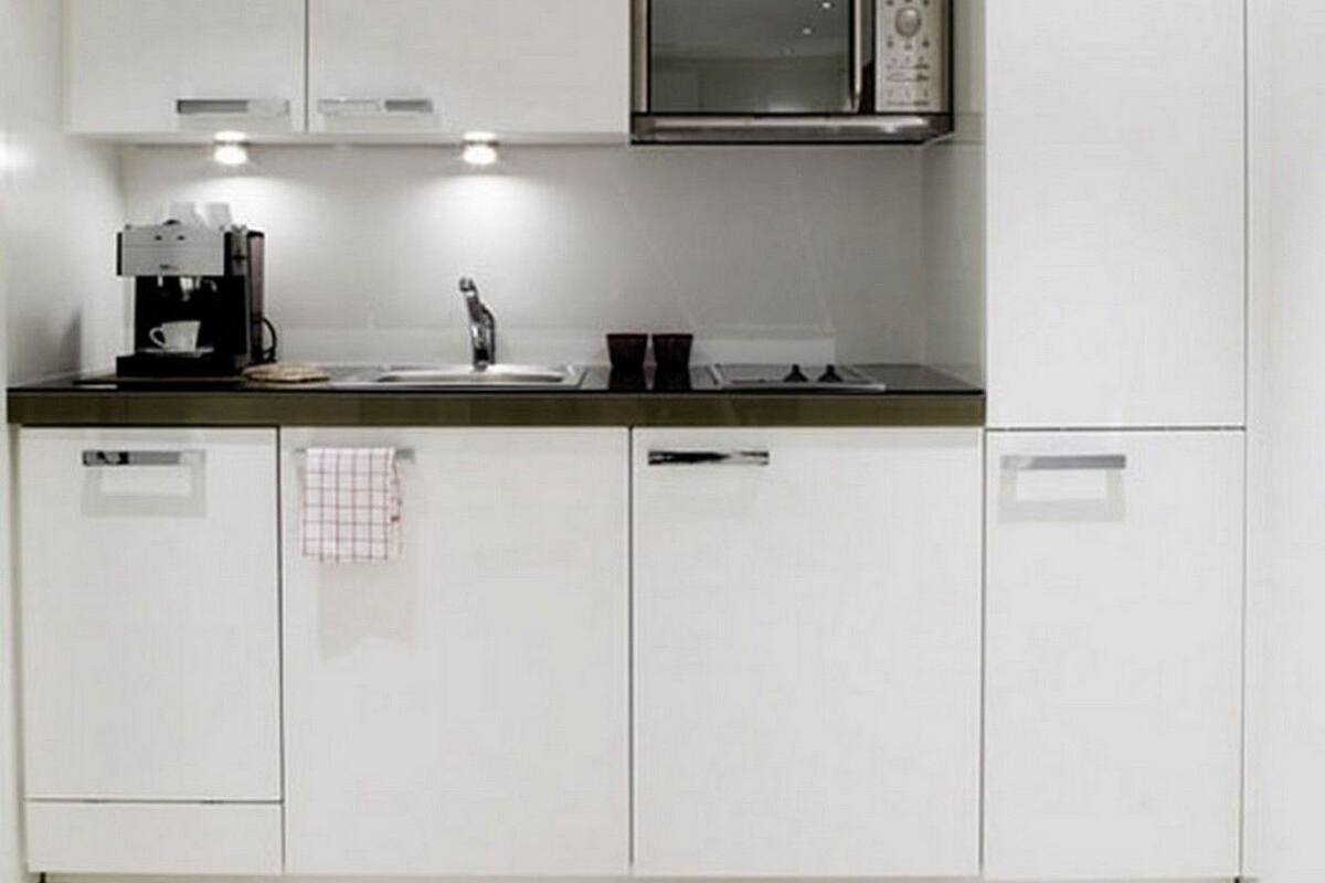 Una cocina moderna con armarios blancos, un microondas de acero inoxidable, una cafetera y un fregadero.