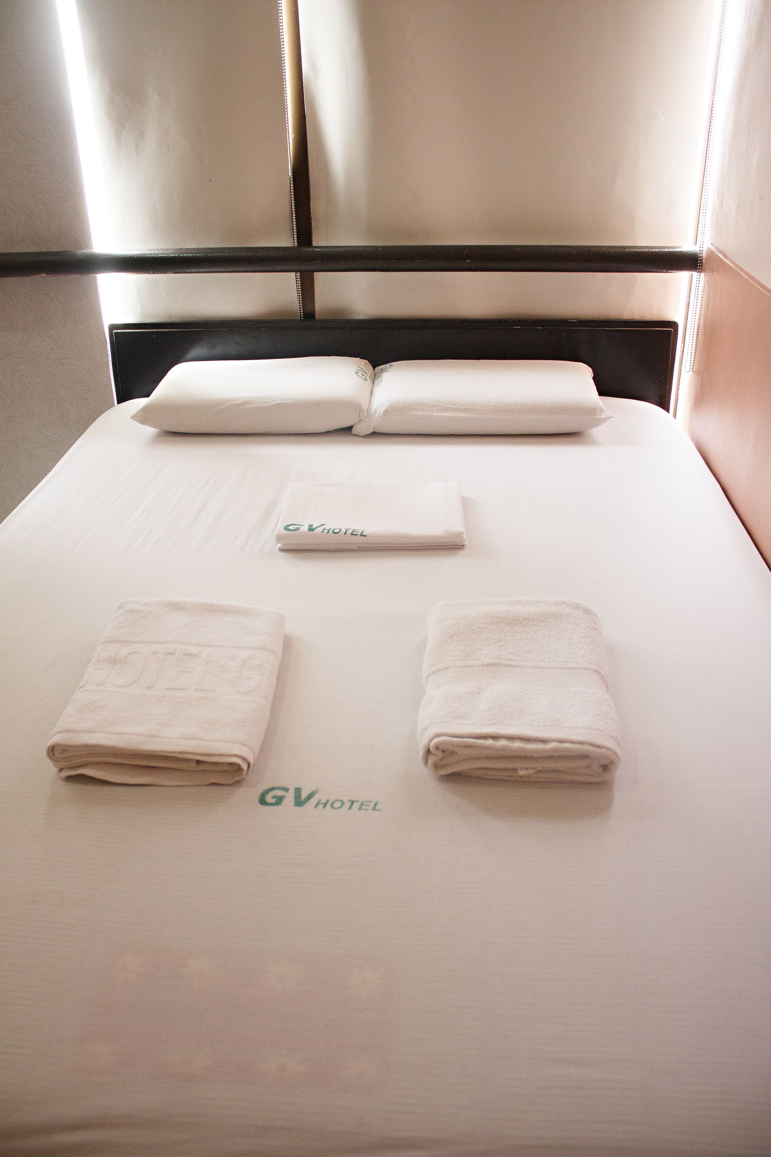 A hotel room with a neatly made bed, pillows, and a folded towel with the hotel logo.