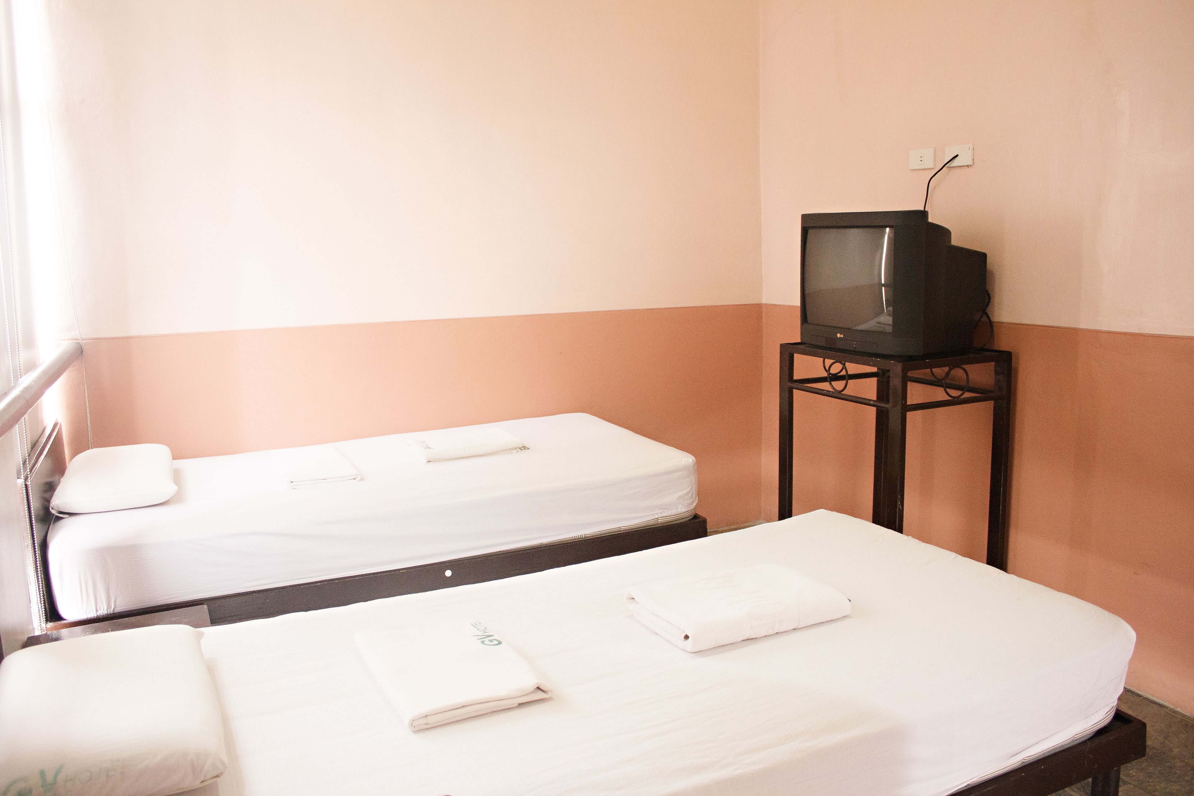 Two single beds with white linens and pillows, a television on a stand, and a wall socket.