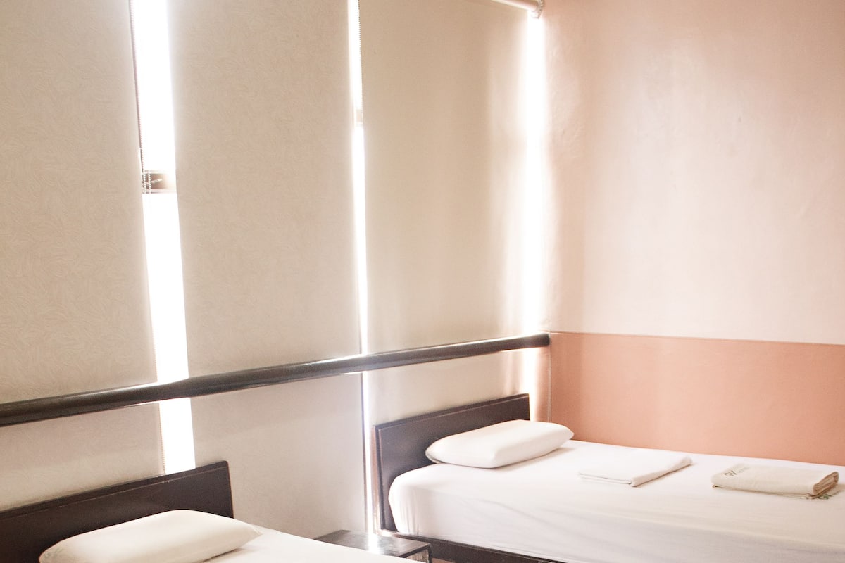 Two single beds with wooden frames and white bedding in a room with tiled flooring and a plain wall.