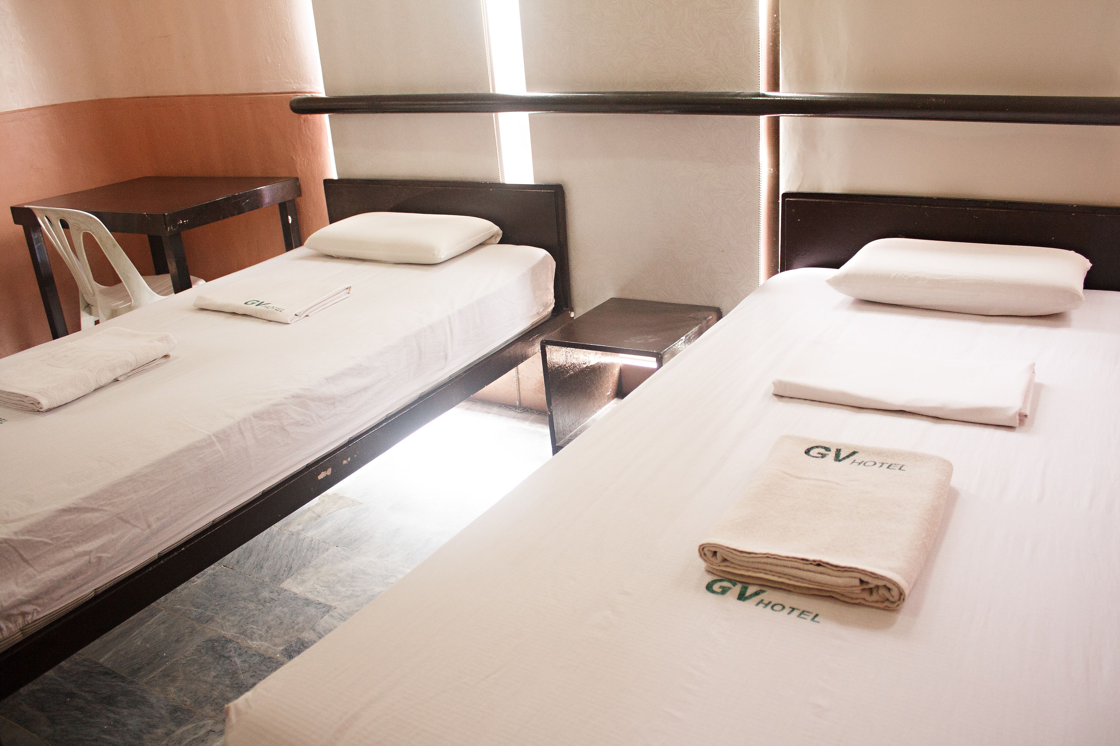 Habitación de hotel con dos camas, cada una con una almohada y una toalla doblada.