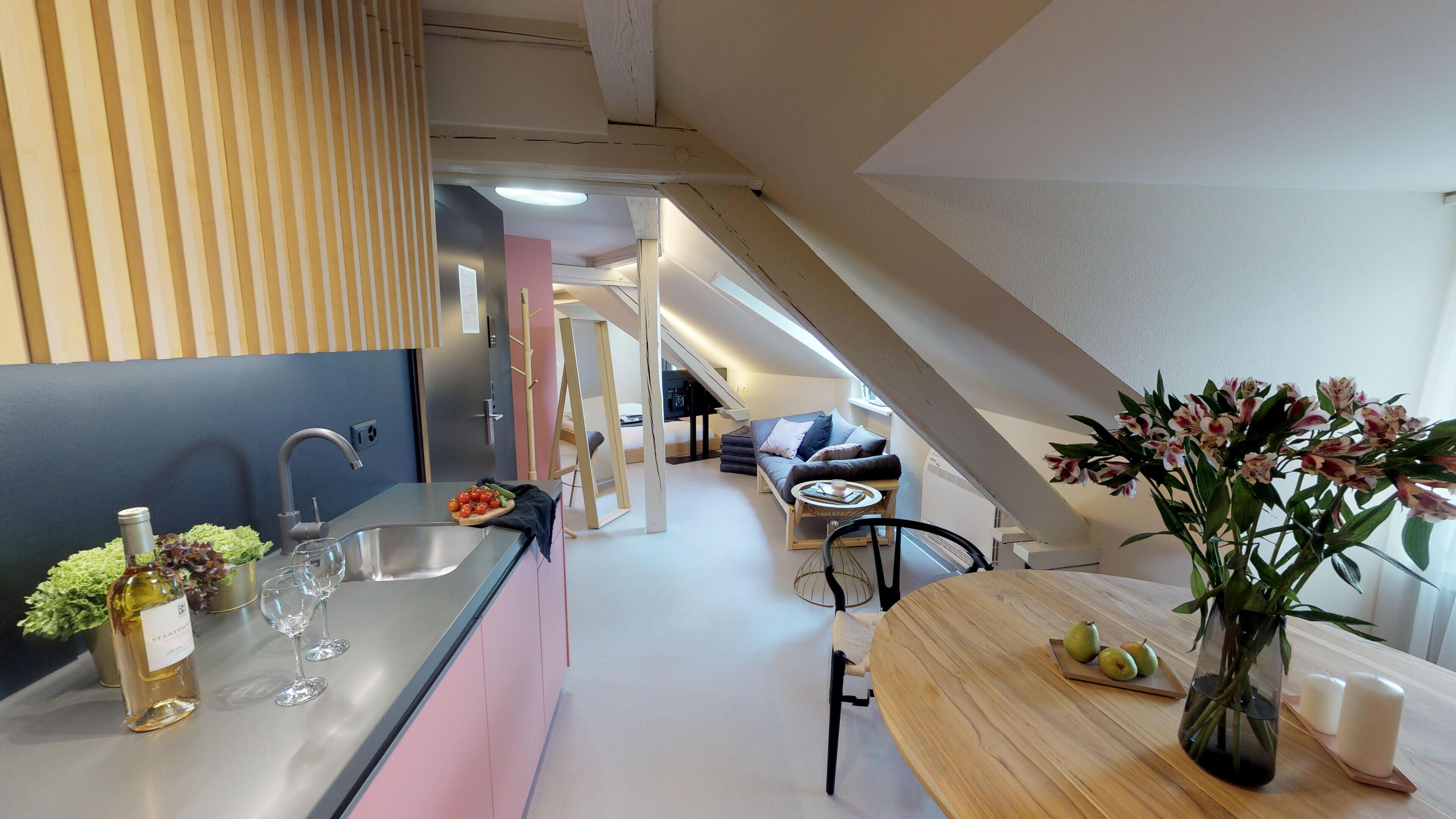 Una cocina moderna con un lavaplatos empotrado, una zona de comedor con una mesa de madera y una escalera que lleva a un nivel superior.