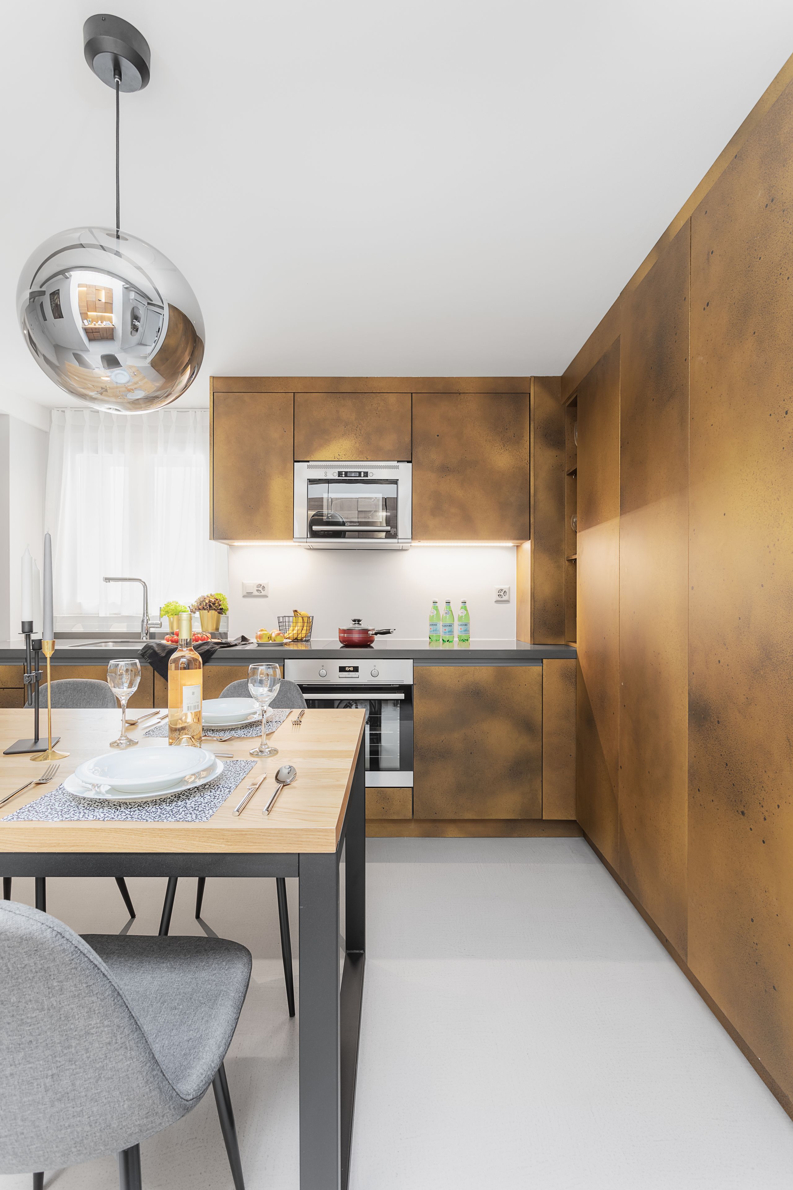 A modern kitchen with wooden cabinets, a stainless steel range hood, and a dining area with a table set for two.