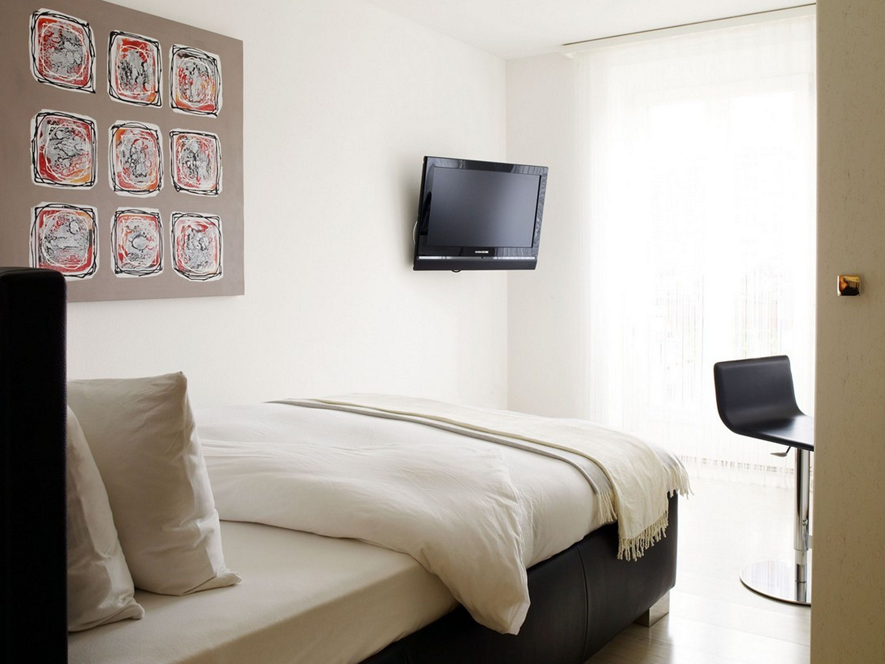 Quarto de hotel moderno com uma cama, televisão de tela plana na parede e uma janela com cortinas.