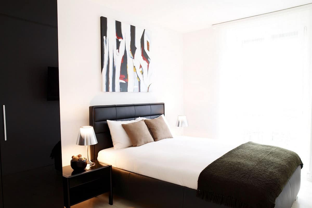 A modern bedroom with a large bed, a nightstand, a lamp, and abstract wall art.