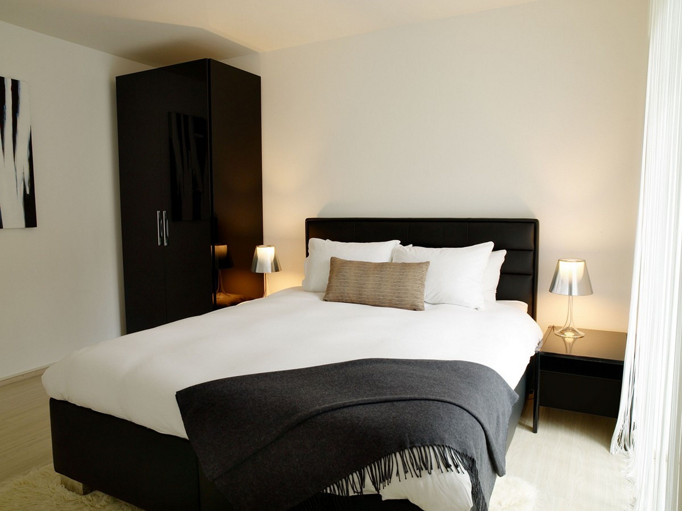 Een moderne hotelkamer met een groot bed, een donker hoofdbord, twee bedlampen, een kledingkast en een groot abstract schilderij aan de muur.