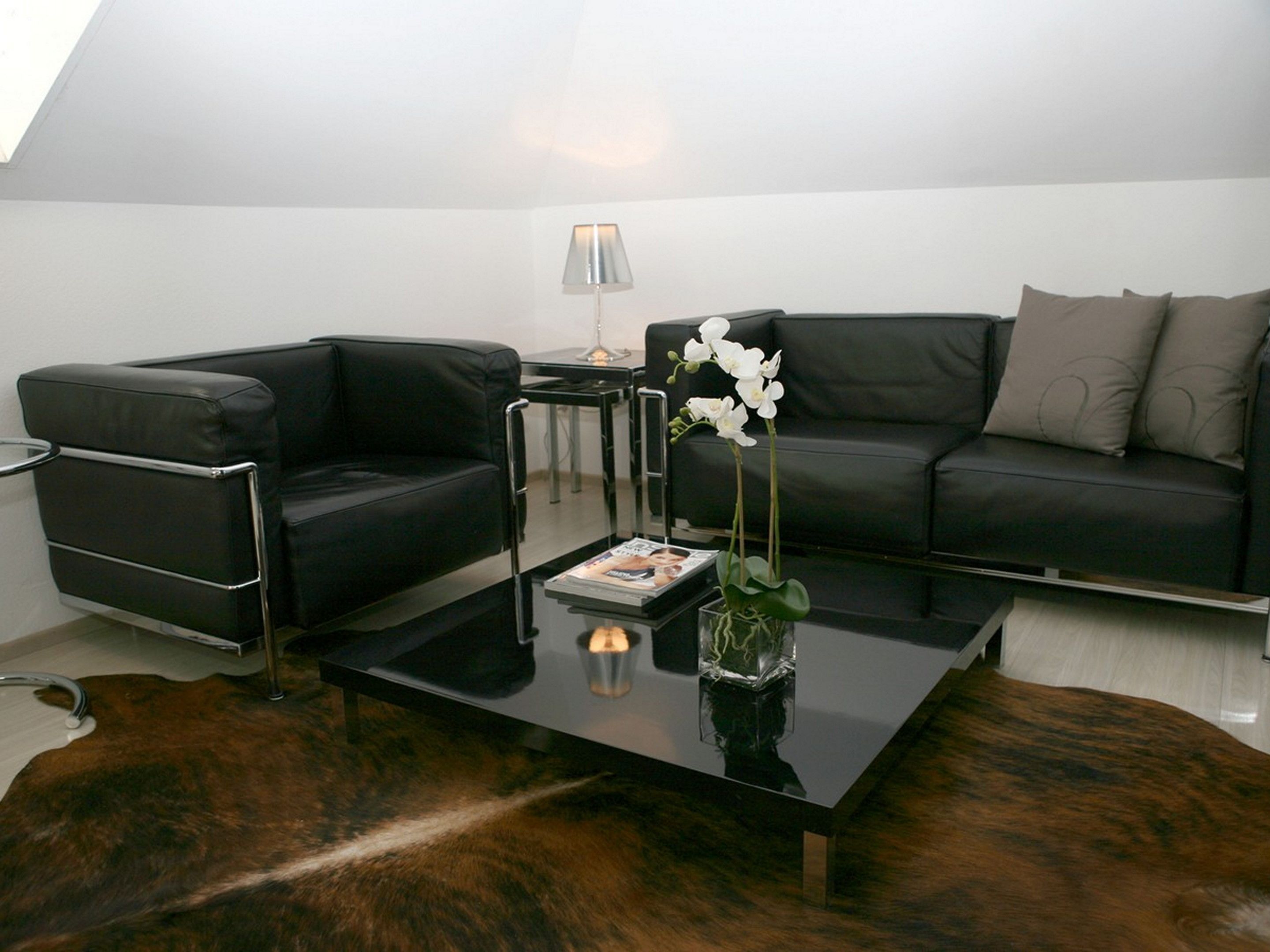 Un salon moderne avec un canapé en cuir noir, une table basse en verre et un vase rempli de fleurs blanches.