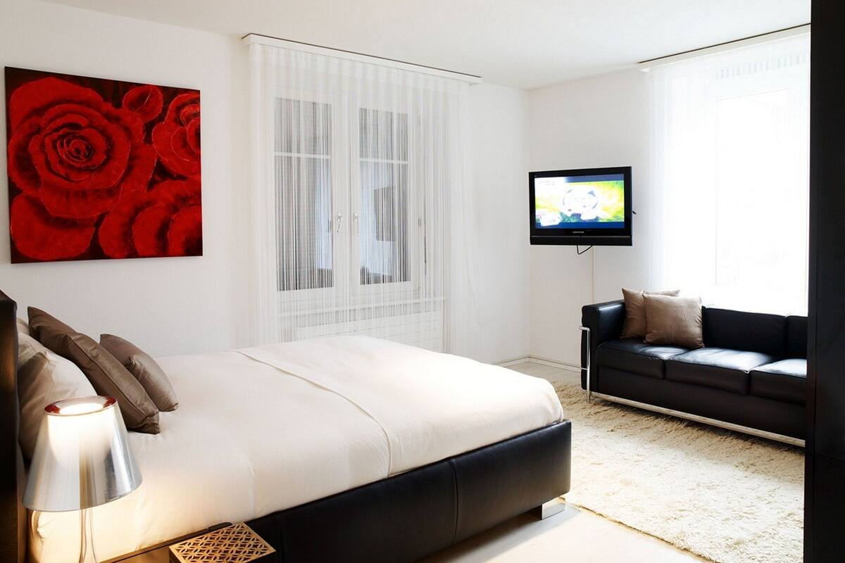 A modern bedroom with a large bed, a TV, a sofa, and a red rose artwork.