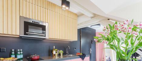 Een moderne keuken met roze kastjes, een ingebouwde oven en een houten plafond.