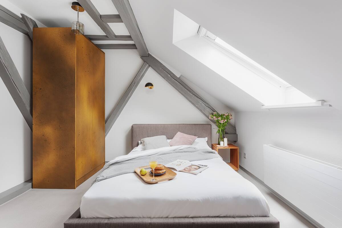 A modern bedroom with a sloped ceiling, a large bed with a tray of breakfast, and a skylight.