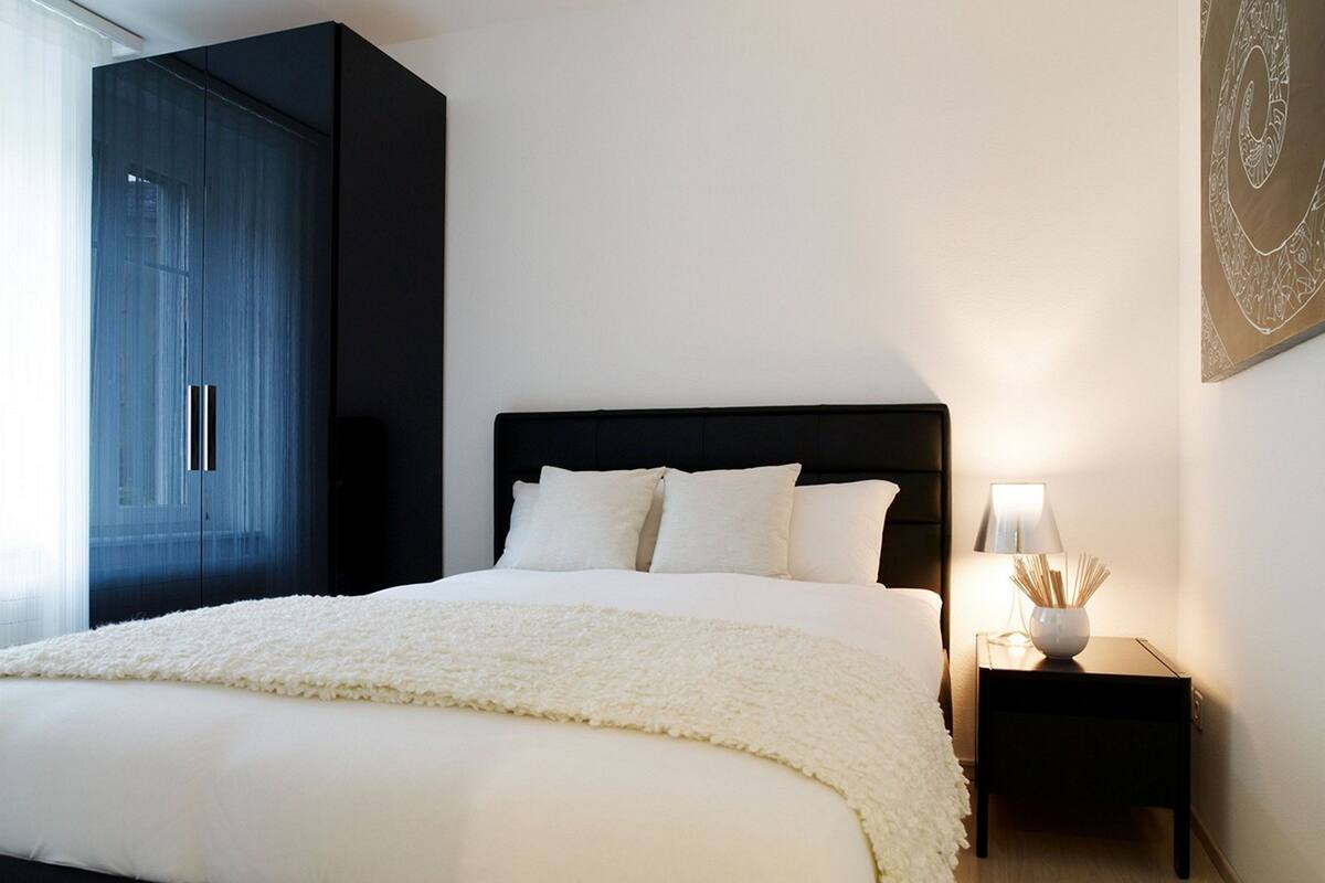 A bedroom with a large bed, a nightstand with a lamp, and a wardrobe.