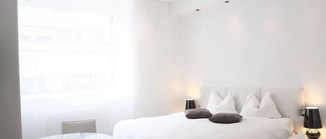 Une chambre d’hôtel moderne avec un grand lit, une table ronde et une vue sur la ville par la fenêtre.