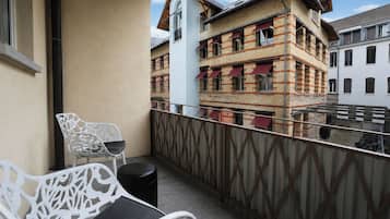 Ein Balkon mit weißem Metallstuhl und kleinem Tisch, mit Blick auf eine Häuserreihe mit roten Markisen.
