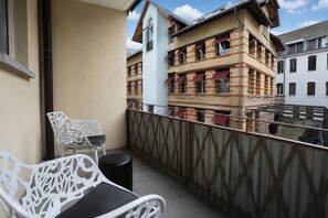 A balcony with a white metal chair and a small table, overlooking a row of buildings with red awnings. - VISIONAPARTMENTS Zurich Freyastraße (Zürich)