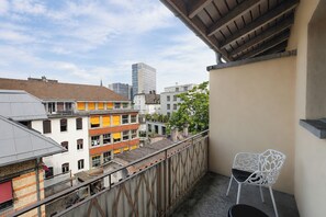 Un balcon avec une rambarde en métal, une chaise blanche et une vue sur les immeubles de la ville.