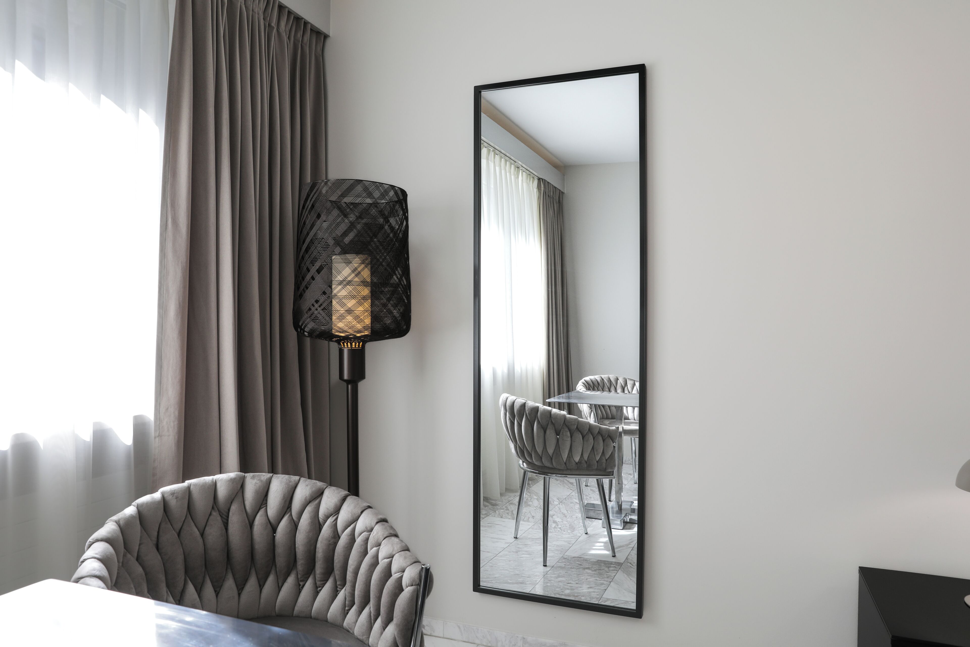 A hotel room with a modern design, featuring a large mirror, a tufted armchair, and a dining table with chairs.