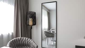 A hotel room with a modern design, featuring a large mirror, a tufted armchair, and a dining table with chairs.