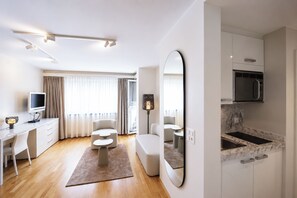Une chambre d’hôtel moderne dotée d’une télévision à écran plat, d’un canapé, d’un coin repas, d’une cuisine avec un four intégré et d’un grand miroir.