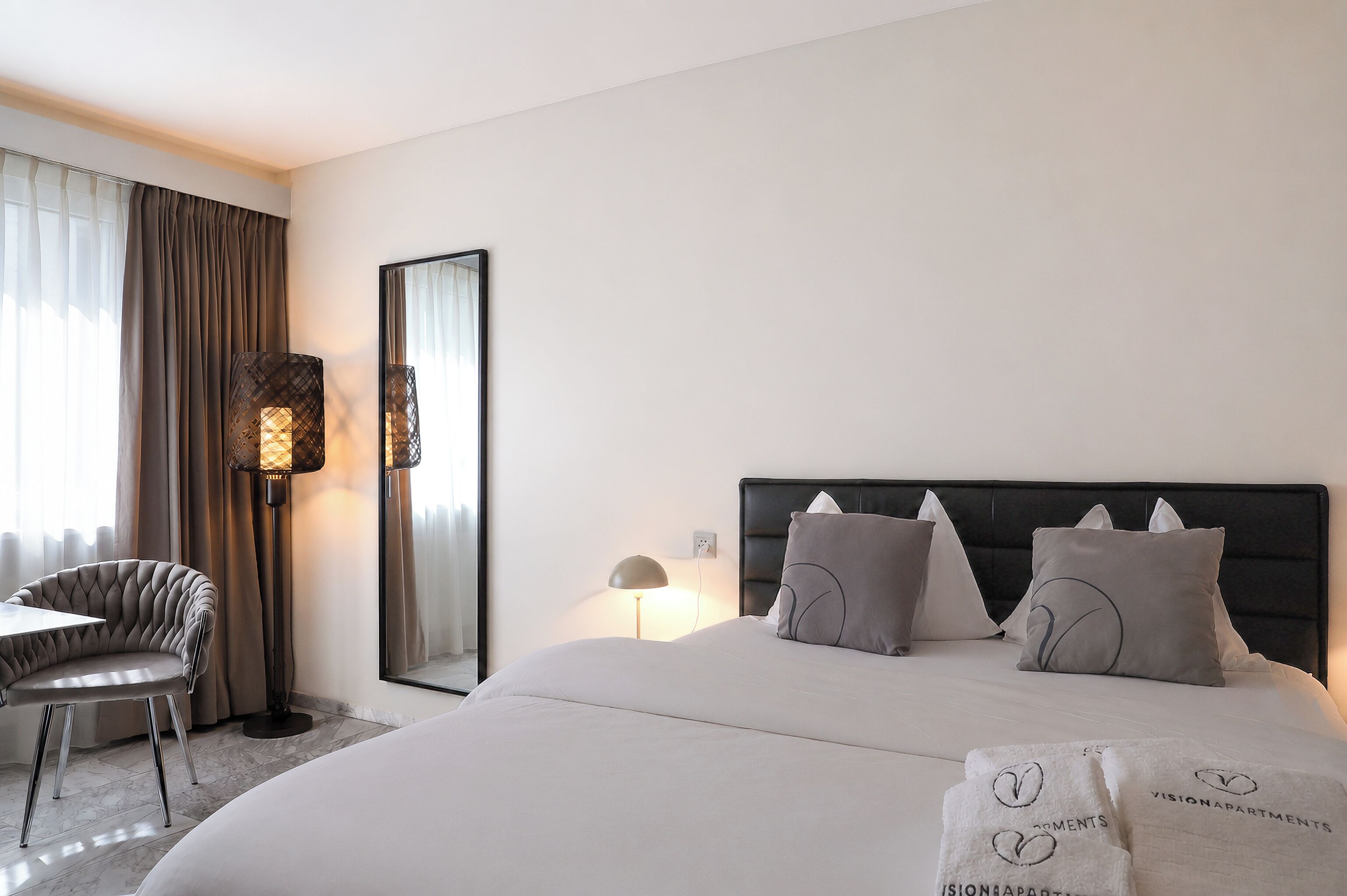 A hotel room with a bed, a chair, a desk, and a large mirror.