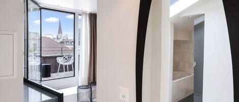Un intérieur moderne avec un balcon, une vue sur la ville et un aperçu d’une salle de bain.