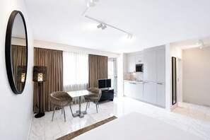 A modern hotel room with a dining area, a kitchen, and a large mirror.