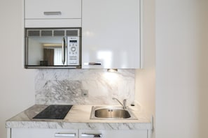 Una cocina con microondas integrado, un lavamanos de acero inoxidable y una encimera de mármol.