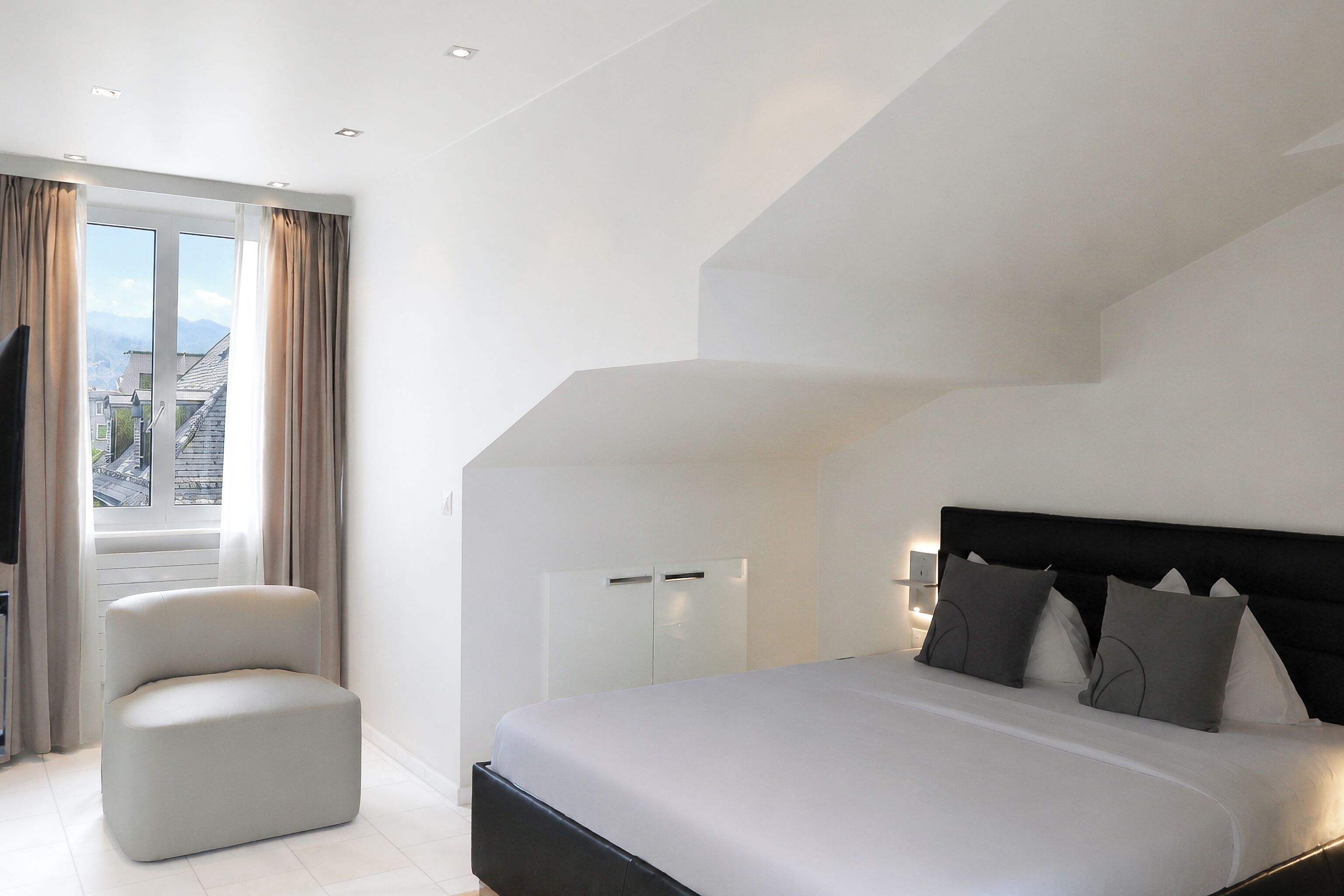Une chambre moderne avec un grand lit, un coin salon et une vue sur le paysage urbain par la fenêtre.