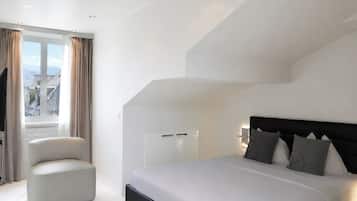 Ein modernes Schlafzimmer mit einem großen Bett, einer Sitzecke und Blick auf die Stadt durch das Fenster.