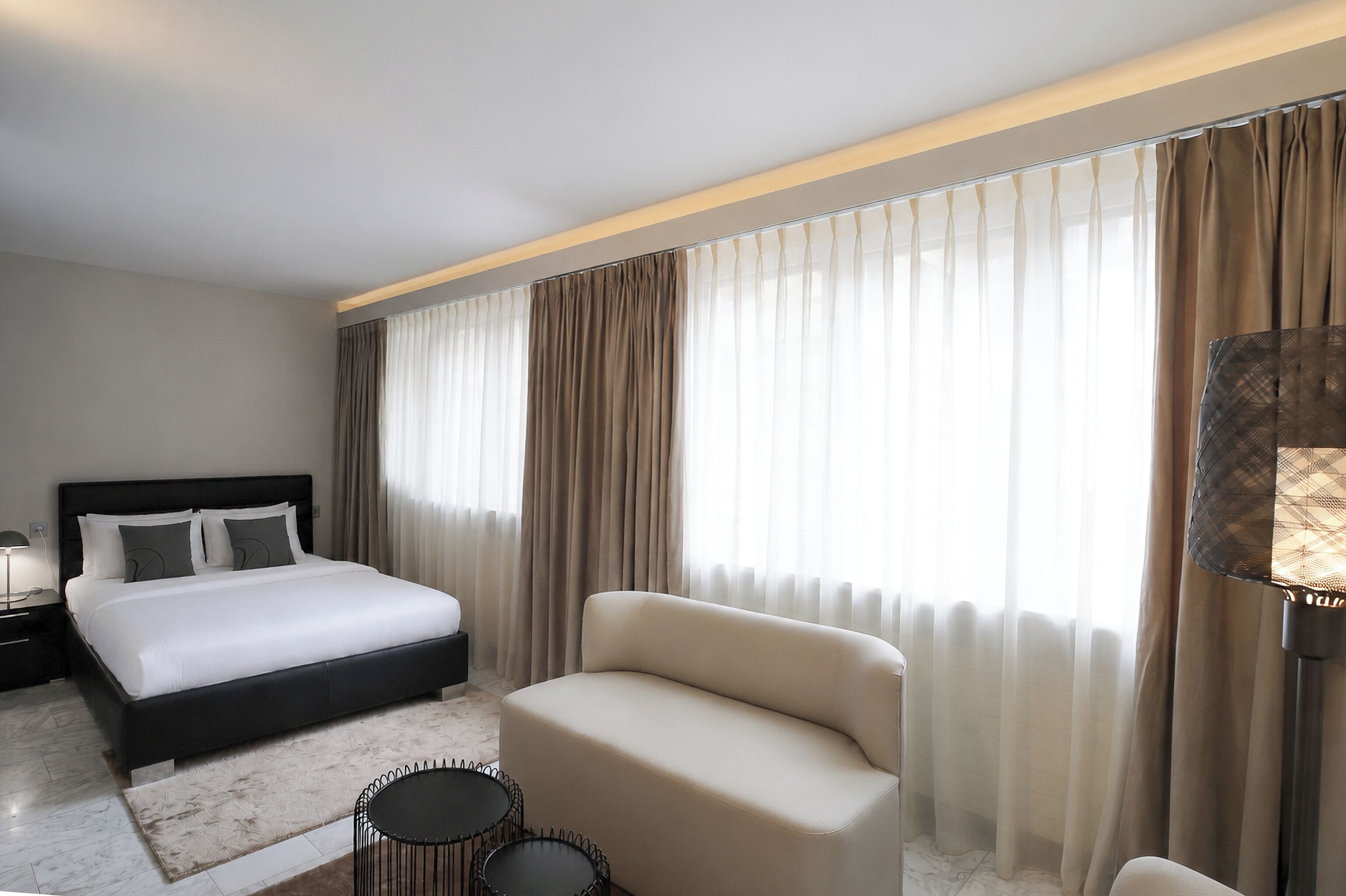 Une chambre d’hôtel moderne avec un lit, un canapé, une petite table et une lampe.