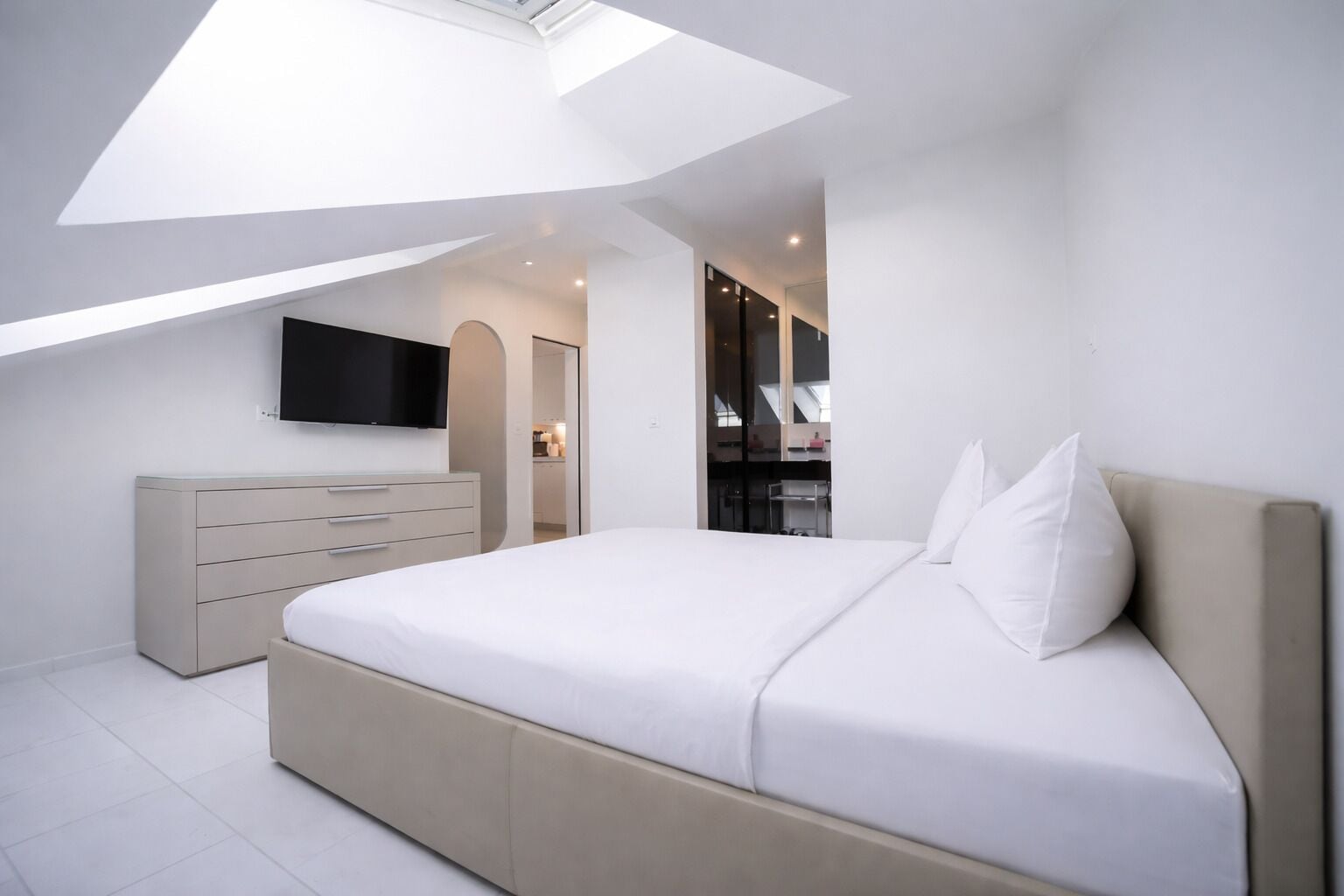 Ein modernes Schlafzimmer mit einer Dachfensterkuppel, einem Flachbildfernseher, einem Bett mit weißer Bettwäsche und einer schlichten Kommode.