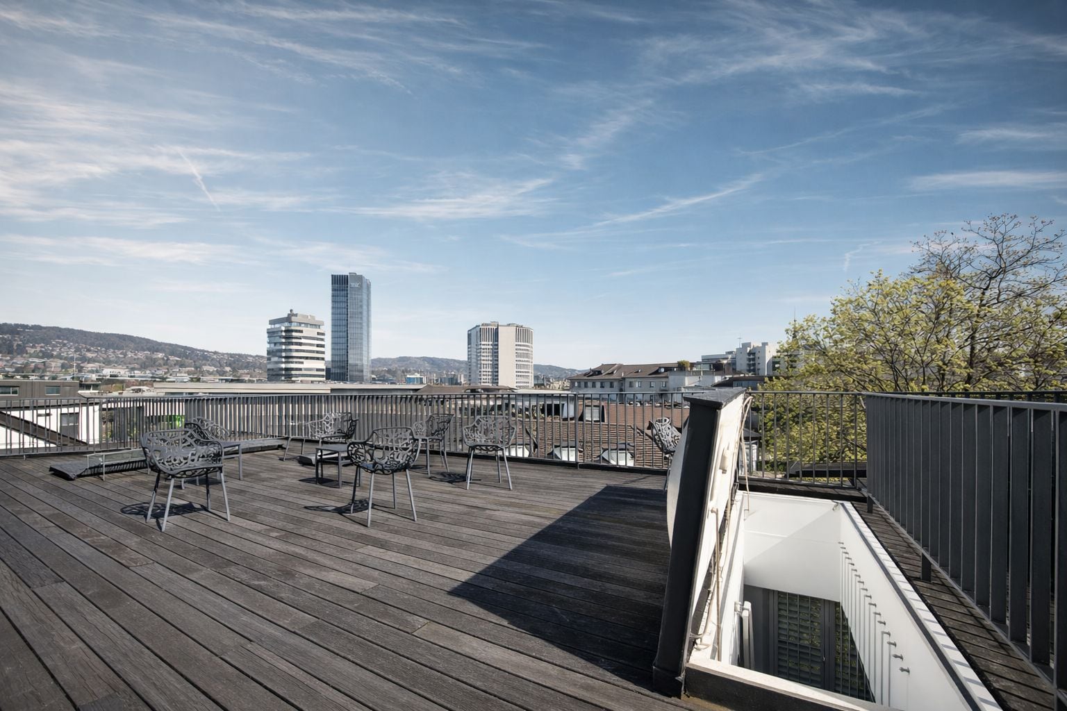 Une terrasse sur le toit offrant une vue sur le paysage urbain, avec des bâtiments modernes et une colline visible au loin.